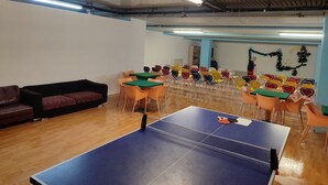 A ping pong table in a room with multiple chairs, a sofa, and a wall with decorations. - Excelsior Hotel Cimone Lowcost (Primiero San Martino di Castrozza)