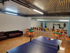 A ping pong table in a room with multiple chairs, a sofa, and a wall with decorations. - Excelsior Hotel Cimone Lowcost (Primiero San Martino di Castrozza)