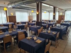 Ein Essbereich mit mehreren Tischen, Stühlen und abgehängten Leitungen.