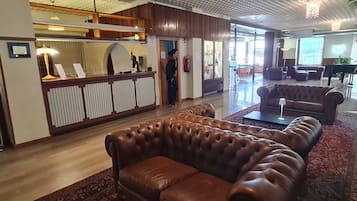 Una hall con una reception, divani in pelle, un tappeto decorato e un pianoforte.