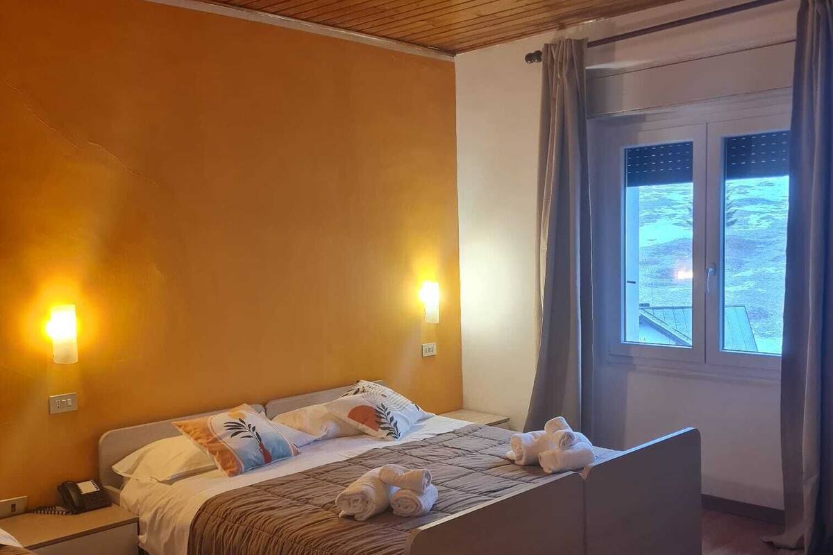 Ein Schlafzimmer mit Holzboden, einem Bett mit Kopfteil, Nachttischlampen, einem Fenster mit Vorhängen und einem kleinen Nachttisch.