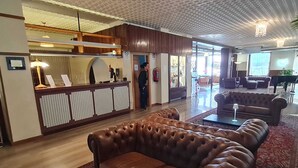 Un vestíbulo con mostrador de recepción, sofás de cuero, alfombra estampada y un piano.