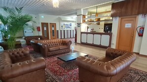 Eine Lobby mit Ledersofas, einem gemusterten Teppich, einem Empfangsbereich und einer Chandelier.