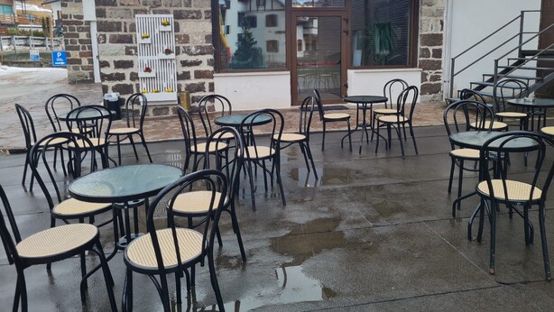 Ein Straäencafé mit Tischen und Stühlen, einer Steinmauer und einem Glastür-Eingang.