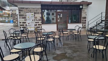 Un caffè all'aperto con tavoli e sedie, un muro in pietra e un ingresso con porta in vetro.