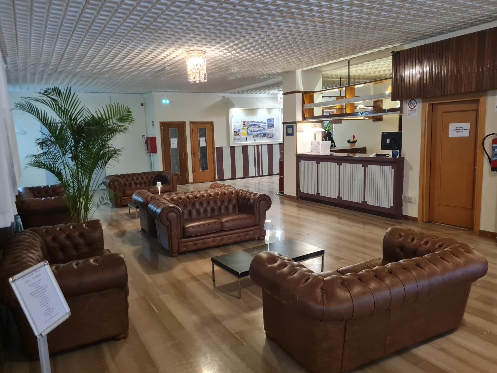 Una hall con divani in pelle, una reception, una pianta grande e un soffitto decorato.