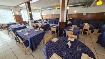 Zona pranzo con tavoli apparecchiati per gli ospiti, sedie in legno e pavimento piastrellato.