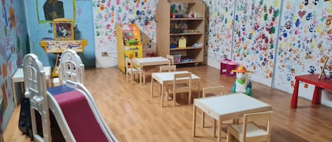 A children's playroom with a slide, tables, chairs, a toy car, and a bookshelf.