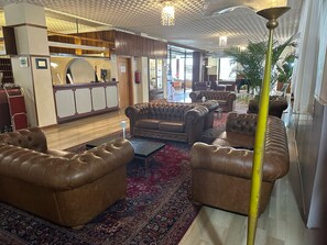 Een lobby met lederen banken, een receptiebalie en een kamerbreed tapijt met dessin.