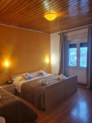 Ein Schlafzimmer mit Holzboden, einem Bett mit Kopfteil, Nachttischlampen, einem Fenster mit Vorhängen und einem kleinen Nachttisch.