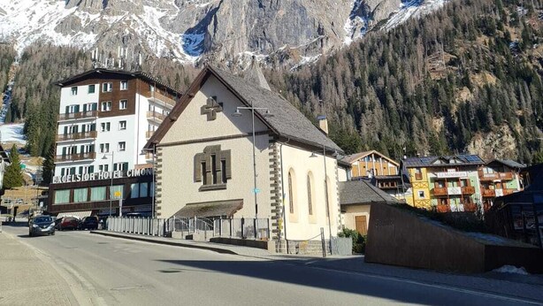 Un pueblo de montaña con un hotel destacado, una iglesia y picos nevados al fondo.