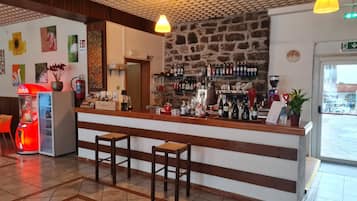 Zona bar con sgabelli, un bancone con diverse bottiglie, un estintore e opere d'arte alle pareti.