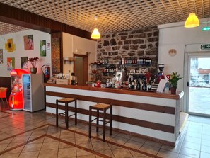 Un espace bar avec des tabourets, un comptoir où sont exposées différentes bouteilles, un extincteur et des œuvres d’art accrochées aux murs.