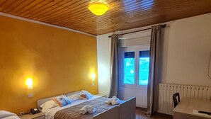 Ein Hotelzimmer mit Holzboden, einem Bett mit Kopfteil, einem Sofa, einem kleinen Tisch und einem Fenster mit Vorhängen.