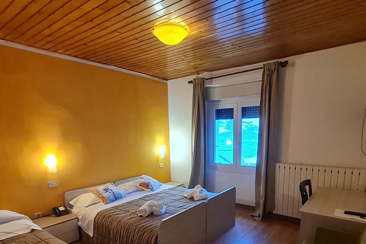 Une chambre d’hôtel avec un plafond en bois, un lit avec une tête de lit, un canapé, une petite table et une fenêtre avec des rideaux.