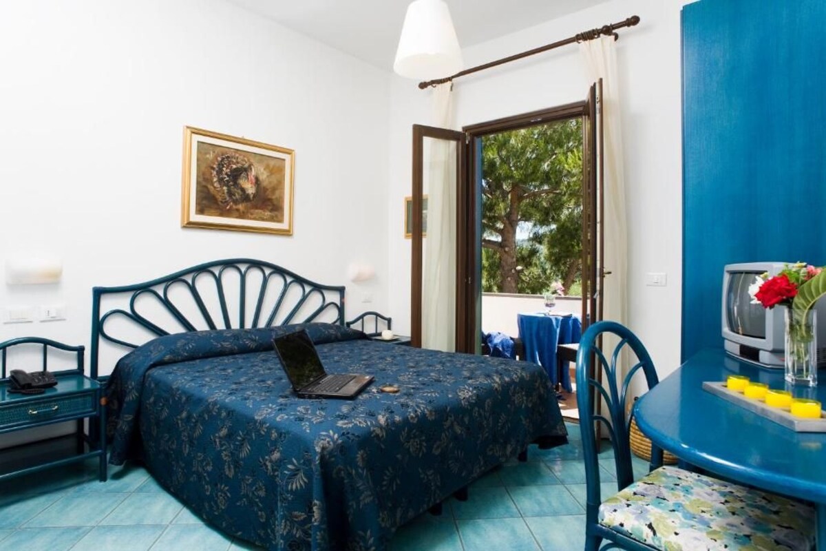 A bedroom with a bed, a laptop, a desk, and a TV.