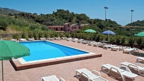A swimming pool with lounge chairs and umbrellas, surrounded by a landscaped area with hills in the background. - Casa Delle Monache Boutique Resort (Castiglione di Sicilia)