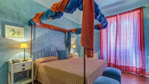 A bedroom with a four-poster bed, a nightstand with a lamp, and a window with red curtains. - Casa Delle Monache Boutique Resort (Castiglione di Sicilia)