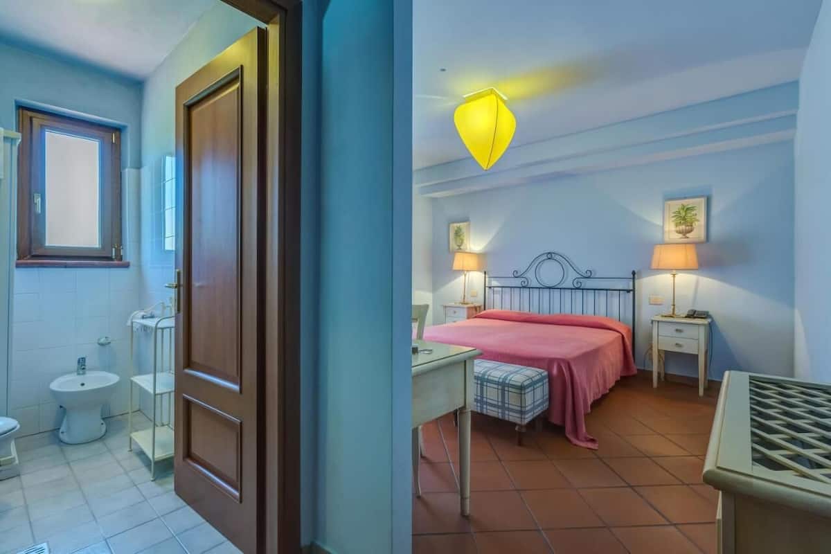 Quarto com cama, mesas de cabeceira, escrivaninha e janela.