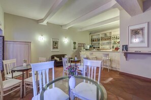 A dining area with a glass table, white chairs, and a vase of flowers. There is a kitchen area with shelves of bottles and a bar counter in the background. - Casa Delle Monache Boutique Resort (Castiglione di Sicilia)