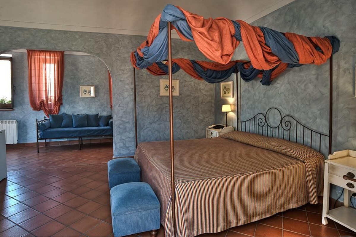 Un dormitorio con cama con dosel, sofá, sillón y mesita de noche.