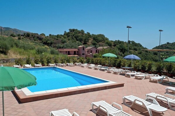 A swimming pool with lounge chairs and umbrellas, surrounded by a landscaped area with hills in the background. - Casa Delle Monache Boutique Resort (Castiglione di Sicilia)