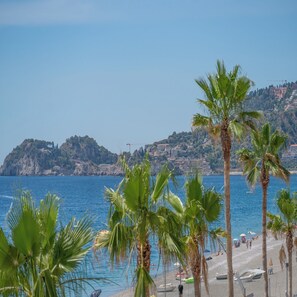 A beach with palm trees, a clear blue sea, and buildings in the background. - Hotel Orizzonte (Letojanni)