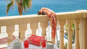Ein Balkon mit Blick auf das Meer, eine Palme sowie ein Tisch mit Gebäck und Getränken.