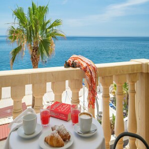 A balcony with a view of the sea, a palm tree, and a table with pastries and drinks. - Hotel Orizzonte (Letojanni)
