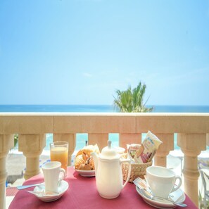 A table with breakfast items, a pitcher, and a cup, set against a balcony with a view of the sea. - Hotel Orizzonte (Letojanni)