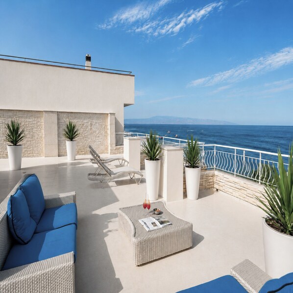 Una terraza en la azotea con sofá, sillones, plantas en macetas y vistas al mar.