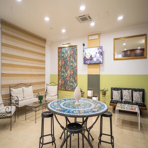 A room with a striped wall, a round table with stools, a sofa, a TV, and a mirror. - Hotel Orizzonte (Letojanni)