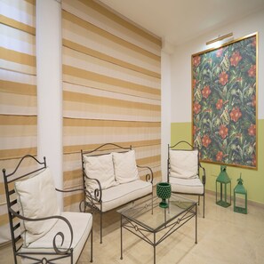 A room with a striped wall, a sofa, two chairs, a glass coffee table, and a floral painting. - Hotel Orizzonte (Letojanni)