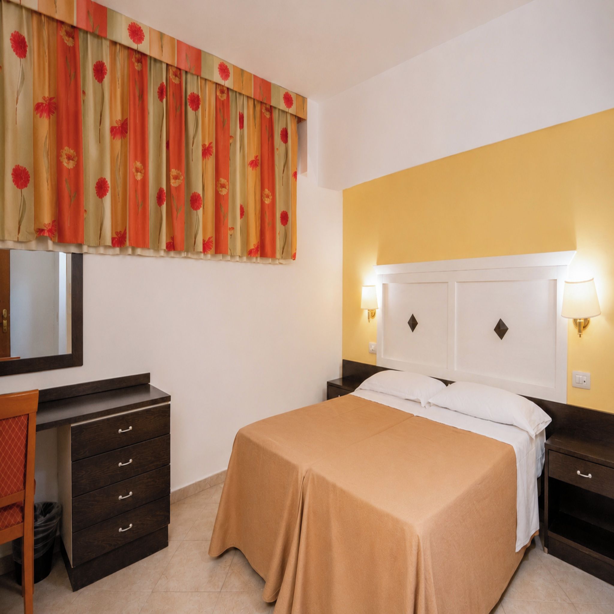 Une chambre d’hôtel avec un lit, des tables de chevet, un bureau et un miroir.