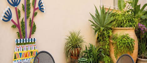 Un patio con una mesa redonda, dos sillas, un adorno de pared y plantas en macetas.