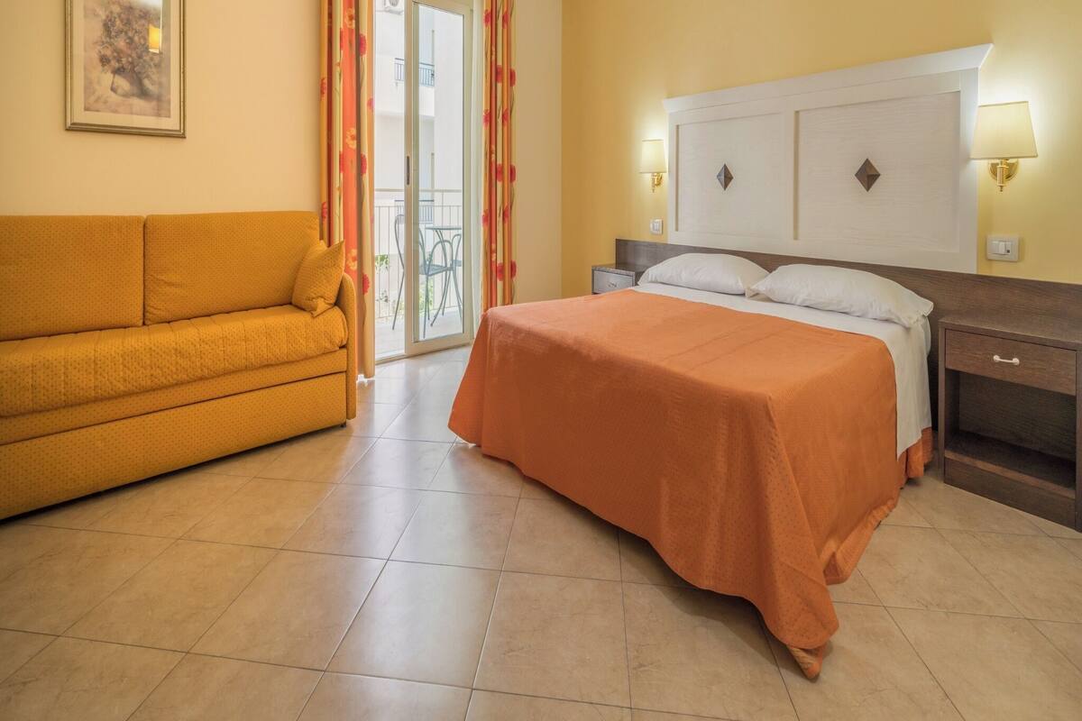 Ein Hotelzimmer mit Bett, Schlafsofa, Nachttisch und einem Gemälde an der Wand.