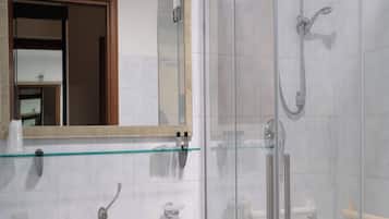 Un bagno con box doccia in vetro, un lavandino con specchio sopra e un portascopevoli.