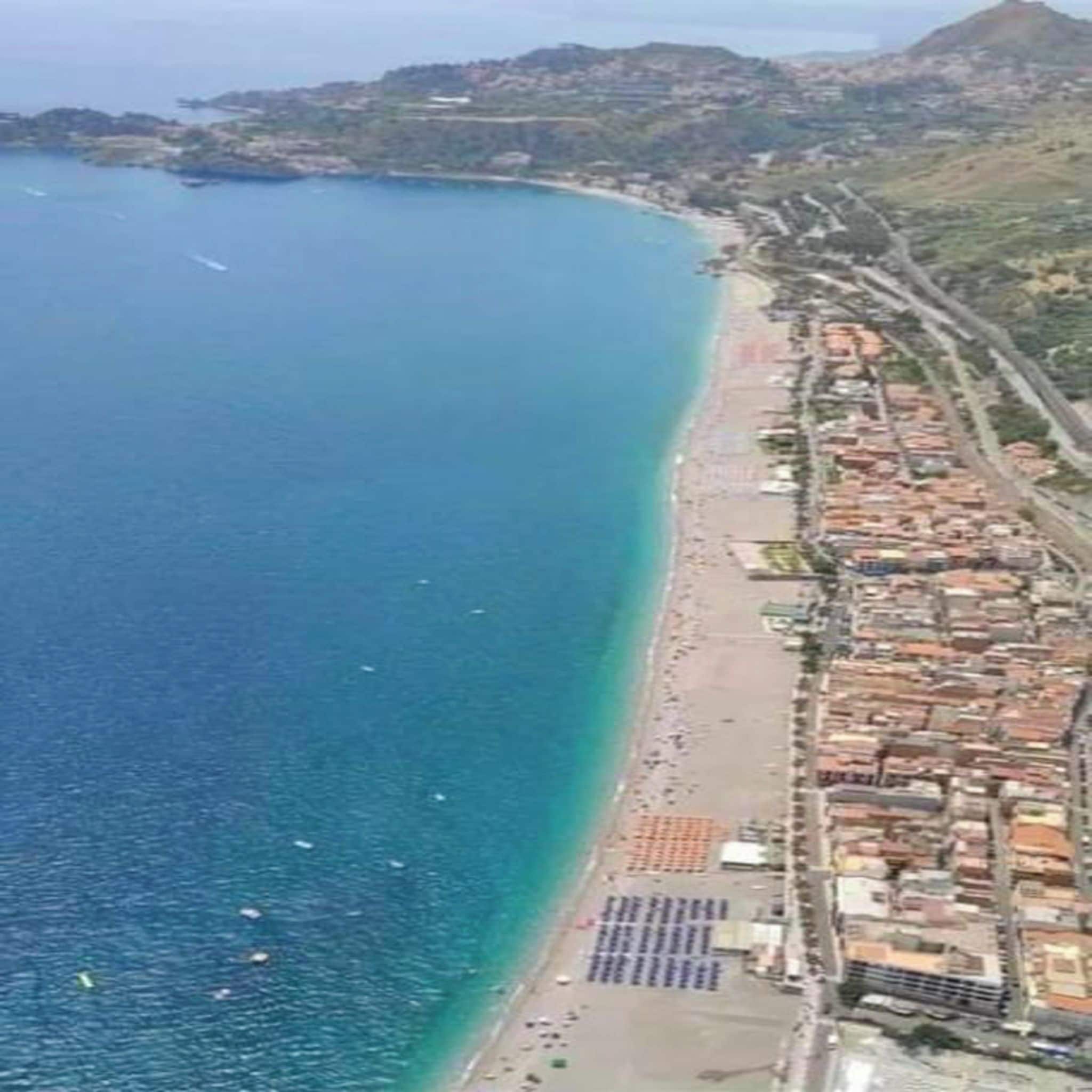Uma área costeira com praia, edifícios e uma paisagem montanhosa ao fundo.