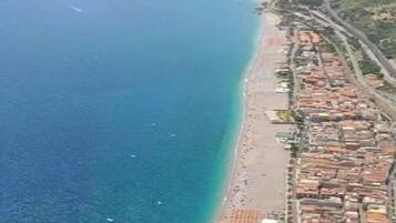 Uma área costeira com praia, edifícios e uma paisagem montanhosa ao fundo.