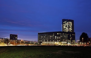 A modern building complex with multiple high-rise structures, illuminated windows, and a well-lit parking area. - UNA Hotels San Vitale Bologna (Bologna)
