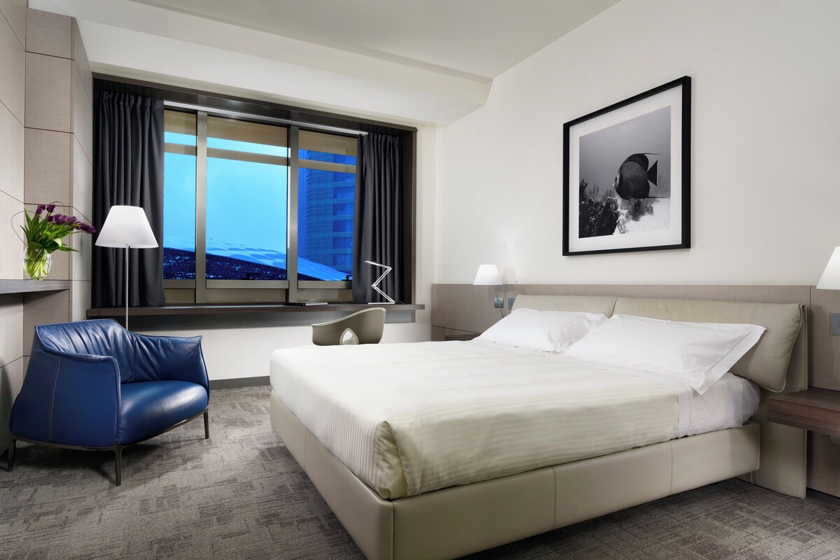 Una habitación de hotel con una cama grande, una silla azul, un escritorio y una ventana con vista a la ciudad.