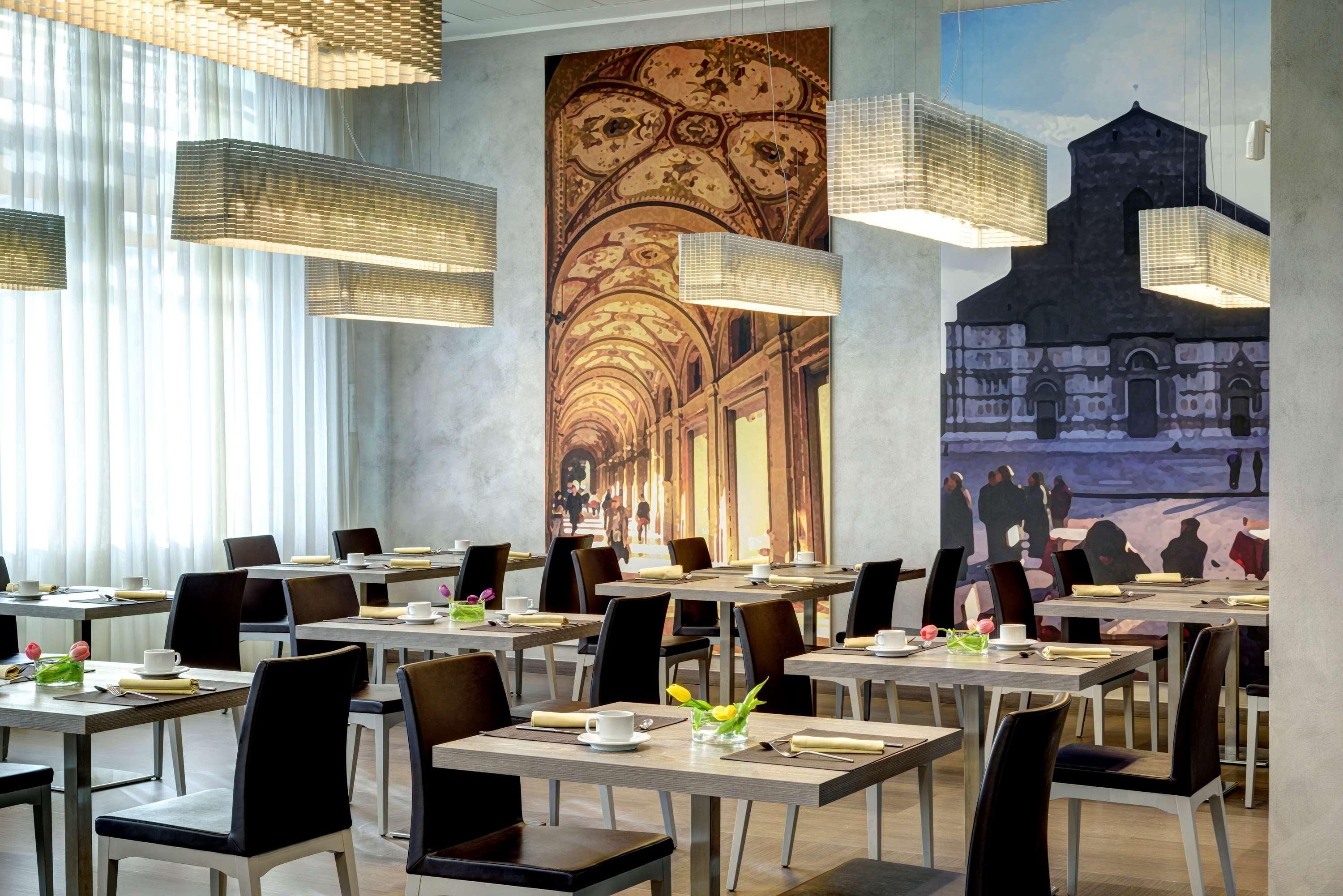 A restaurant with tables set for dining, featuring a mural of a street scene and hanging pendant lights.