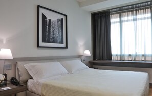 Ein Hotelzimmer mit einem großen Bett, zwei Nachttischlampen, einem gerahmten Bild an der Wand und einem Fenster mit Vorhängen.