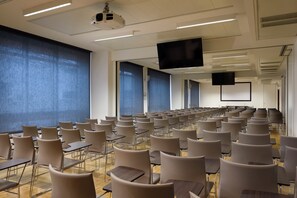 Konferenssihuone, jossa on riveissä tuoleja, projektori ja valkokangas.