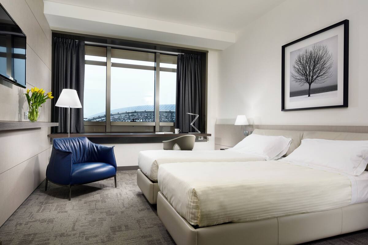 Une chambre d’hôtel avec un grand lit, une chaise, un bureau, une lampe et un tableau encadré au mur.