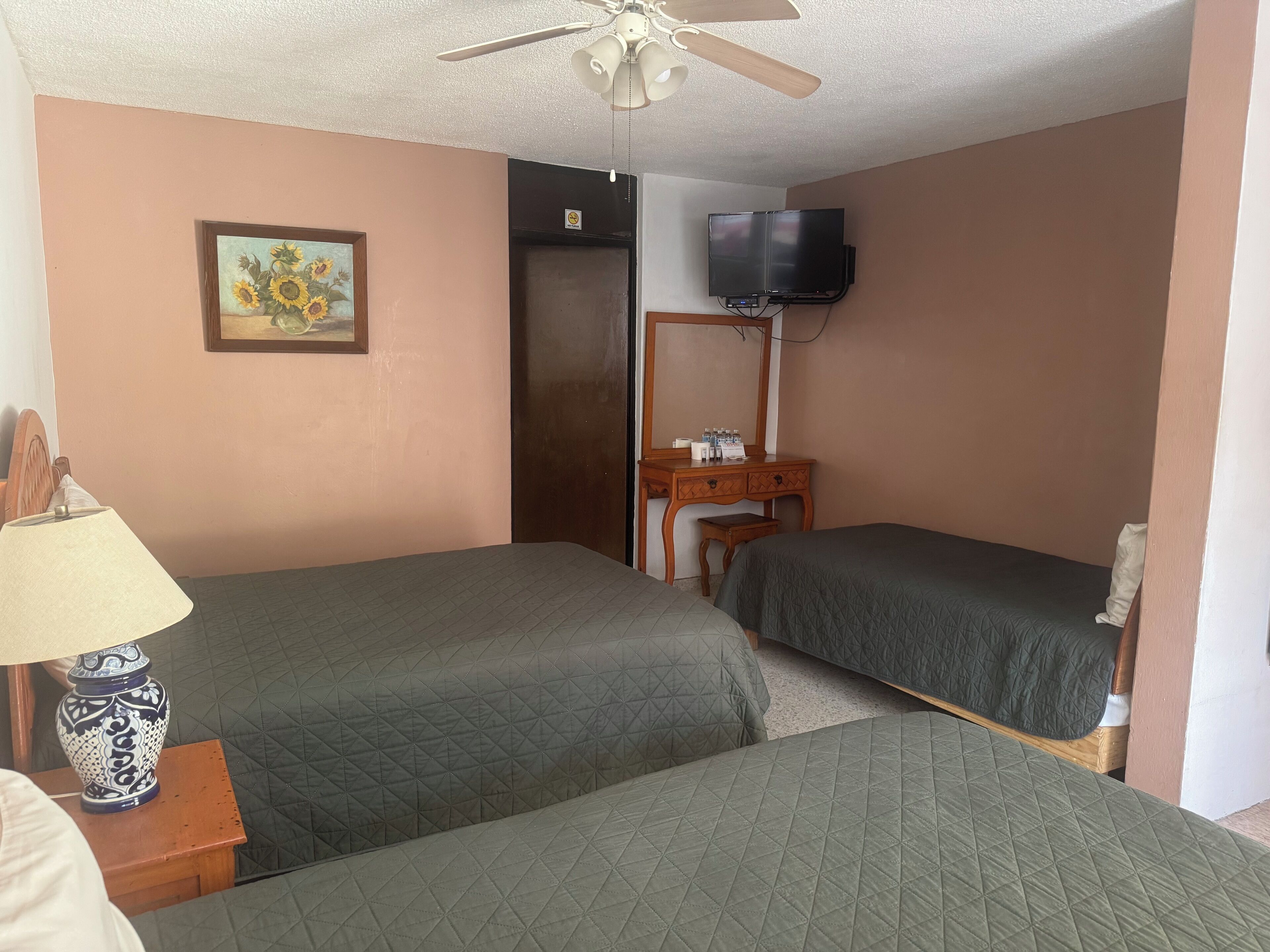 A hotel room with two beds, a television mounted on the wall, a wooden dresser, and a ceiling fan.