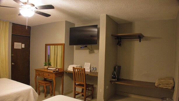 A hotel room with two beds, a desk with a chair, a television mounted on the wall, a small shelf, and a ceiling fan. - Hotel Mesón del Bosque  (Querétaro)
