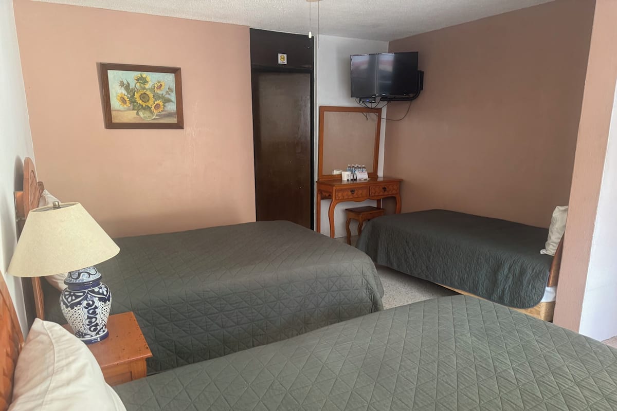 A hotel room with two beds, a TV mounted on the wall, a wooden dresser, and a painting on the wall.