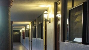 A long, narrow hotel corridor with doors on one side and windows on the other, illuminated by wall-mounted lights. - Hotel Mesón del Bosque  (Querétaro)