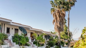 Un hôtel moderne à la façade blanche, doté d’un toit en tuiles de couleur terre cuite et d’un jardin bien entretenu agrémenté de palmiers et d’arbustes.